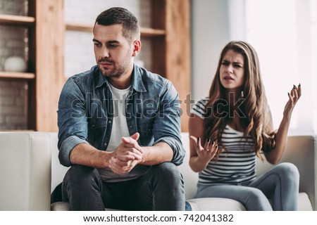 Upset couple at home. Handsome man and beautiful young woman are having quarrel. Sitting on sofa together. Family problems. Royalty-Free Stock Photo #742041382