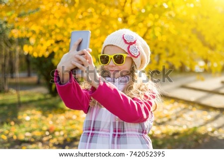 Pretty girl of 7 years doing selfie using a smartphone, autumn background.