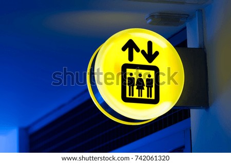 Bright yellow lift or elevator symbol, sign on blue wall background with neon light. Copy space