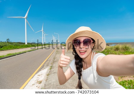 happy Asian woman make thumbs up to agree with green energy windmill power with her holiday trip