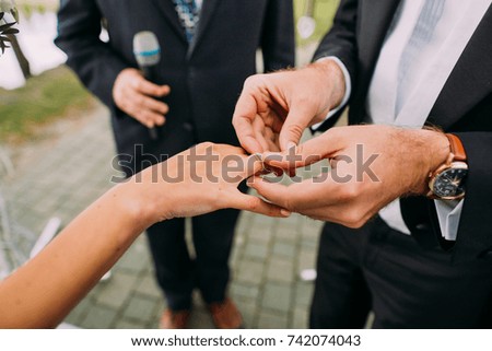 Open air wedding ceremony. Groom puts the wedding ring on the finger of the bride.