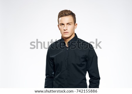 business man in black shirt looks at the camera on a light background                               