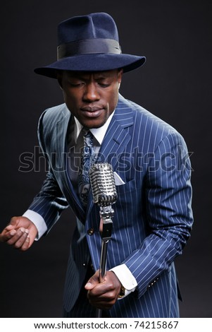 Black man with blue striped suit and blue hat singing.