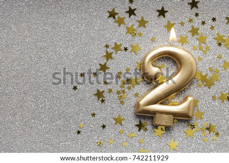 Number 2 gold celebration candle on star and glitter background Royalty-Free Stock Photo #742211929