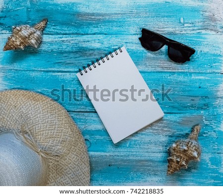 Bright background with painted blue, blue paint boards, sunglasses, straw hat, an open notebook with white page and seashells. Top view