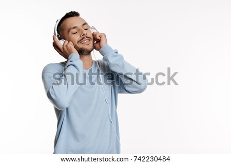 Pleasant dark-haired man listening to music in headphones