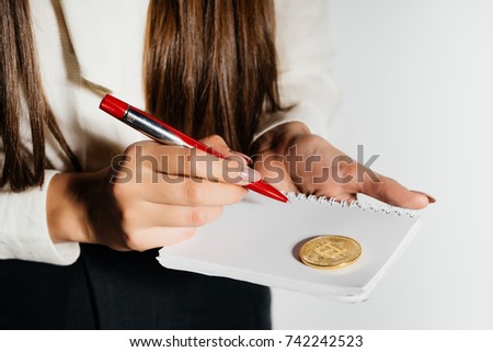 a young modern successful business lady holding a gold bitcoin and a notebook with a pen, thinking about crypto currency