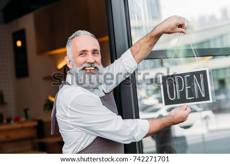 portrait of smiling senior worker putting open chalkboard on cafe door