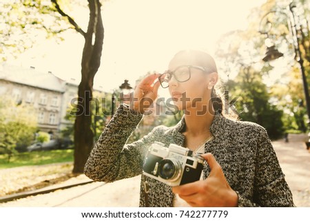 Stunning young woman stands with a camera in a sunny park