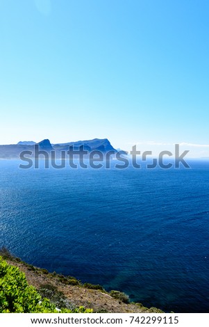 Scenic panorama landscape/seascape photography taken at the Cape of Good Hope near Cape Town, South Africa with blue clear sunny sky and water,light clouds,mountains, fog on the horizon and a bush