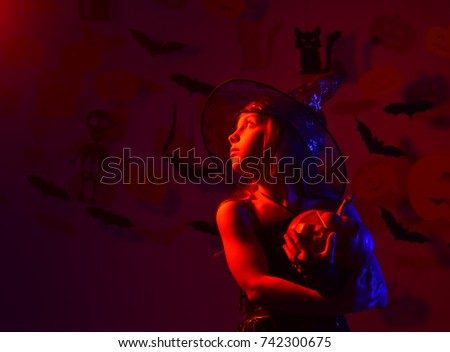 Kid in spooky witches costume holds jack o lantern. Halloween party and decorations concept. Little witch wearing black hat. Girl with dreamy face on bloody red background with bats and pumpkins decor