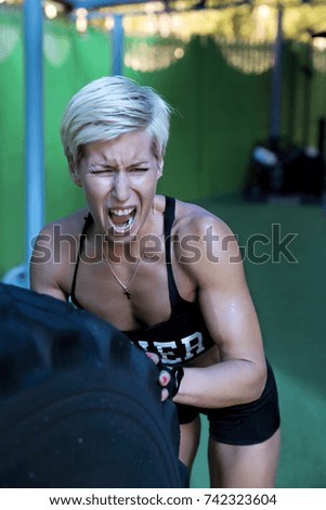 The bodybuilder girl pushes the car wheel in the gym.