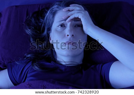 Middle aged woman lying awake in her bed at night because of insomnia, stress, fears, nightmares or illnesses like fibromyalgia Royalty-Free Stock Photo #742328920