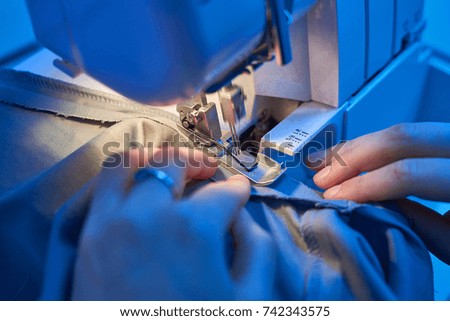Women's hands behind her sewing machines and needle sews fabric textile phase of over stitching close up