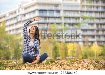 Beautiful girl relaxing and listen music in the city park on blurred background.
