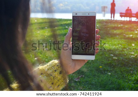 Hand of a Brunette Girl Holding her Mobile Phone in Vertical Orientation While Taking Selfie Photo at the park.