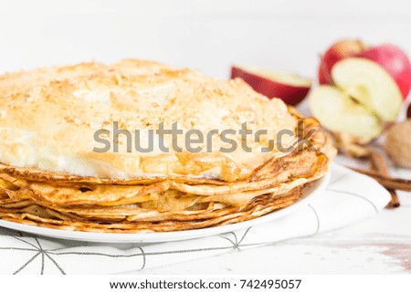 Stack of crepes with meringue on top, served on white plate, apples in the background, Front view.