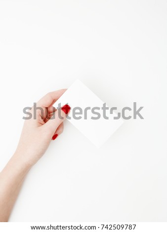 Flat lay, top view. Beauty and fashion concept. Beautiful female hands with red manicure. Minimal style. Minimalist photography. Pale composition with girl's hand holding card on white background