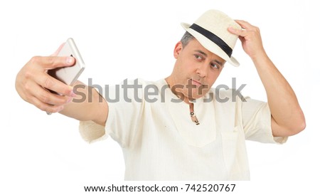 Man uses his cell phone to take a picture. Selfie. He is wearing a white hippie robe. Folk clothes and panama hat. Isolated.