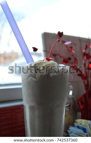 front portrait vertical photography of a beautiful delicious cold frozen fresh milkshake smoothie with whipped cream on top and a candy fruit berry red cherry with a light purple straw 