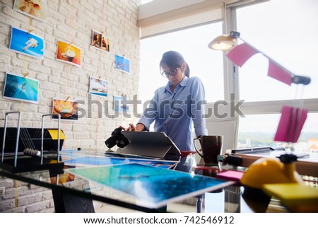 Young people, small business, technology. Woman at work as photographer in office. Hispanic girl using computer laptop for image review, editing.