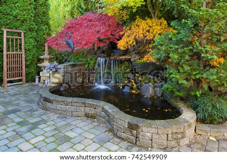 Home garden waterfall pond with brick paver stone hardscape and trees in fall season colors Royalty-Free Stock Photo #742549909