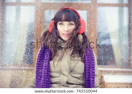 Winter portrait of a young woman. Beauty Joyous Model Girl drawing a hand, winter red headphones, having fun in the winter. Beautiful young woman looks outdoors. Enjoying nature, snow falls in winter