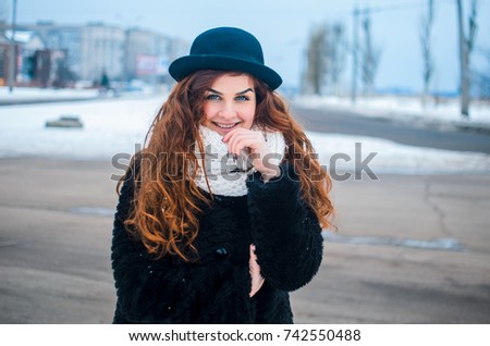 a young girl walks , the girl cerca hat and coat.  Dressed in winter clothes, she has blue eyes and thick red hair . Hair curls , the color of fire .