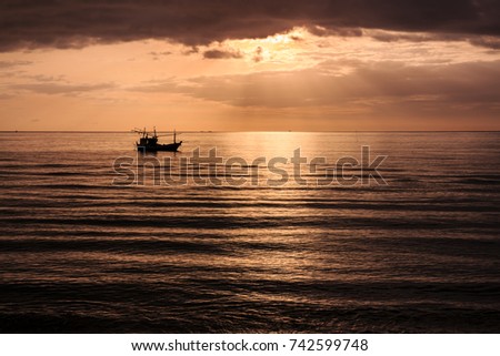 Silhouette of fishing boat at sunset with the beam of sun shines on the surface of the sea