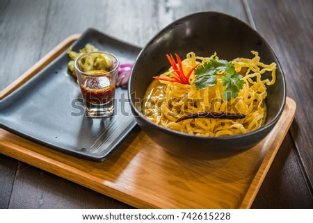 Thai northern traditional style noodle in curry with red onion, pickle and a glass of oil chili on wooden plate on table Royalty-Free Stock Photo #742615228