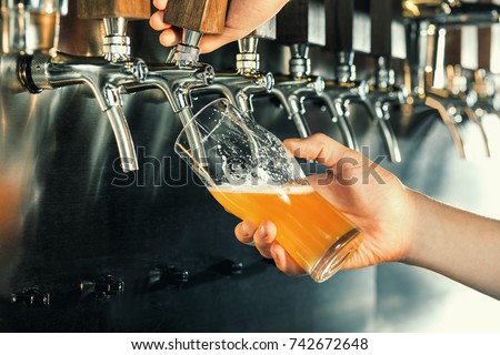 Hand of bartender pouring a large lager beer in tap. Royalty-Free Stock Photo #742672648