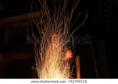 Sparks of a bright fire against the background of a black night. Silhouette of the canting man behind the fires of a bright flame. The witch conjures at the fire at night.