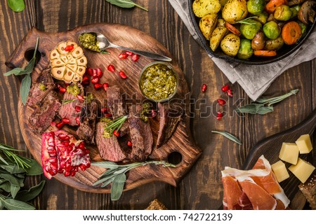 Kangaroo meat steak with green pesto and pomegranate on wooden cutting board. Healthy holiday food concept. Top view.