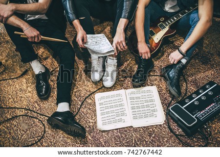 Repetition of rock music band. Cropped image of guitar players and drummer are sitting on the floor at rehearsal base with notes. Top view Royalty-Free Stock Photo #742767442