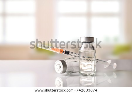 Vials with medication and syringe on white methacrylate table with window background. Horizontal composition. Front view. Royalty-Free Stock Photo #742803874