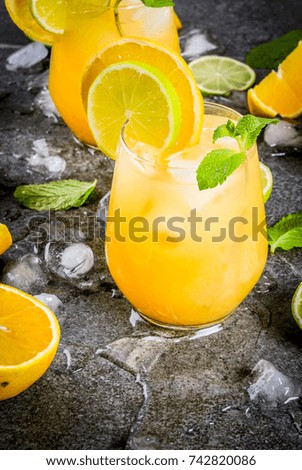 Vitamin summer refreshing drinks. Citrus punch with oranges and lime, with mint sprigs, chilled with ice. On black stone table, with ingredients, copy space