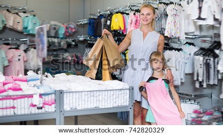 Cheerful woman with daughter choosing dress in the shop with packages