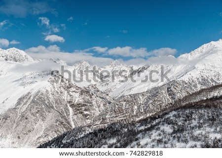 Beautiful mountain peaks covered with clear white snow under the bright blue sky with clouds