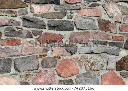 Stonework wall in rows with mortar in reds, browns and grays