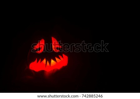 Halloween pumpkins smile and scrary eyes for party night. Close up view of scary Halloween pumpkin with eyes glowing inside at black background. Selective focus