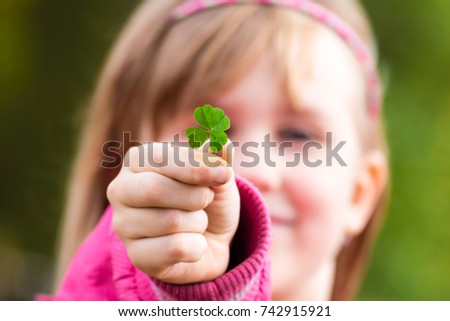 Four leaf clover in small hand of young girl in front of her face. Girl's face on background. Selective focus.