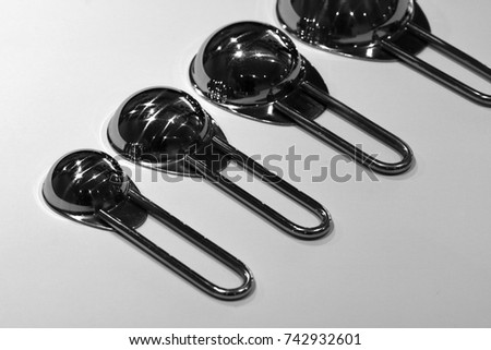 Abstract black and white macro close up photograph, of well used stainless steel measuring spoons, with shadows and grey tones. 2017