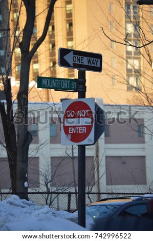 vertical photography of an urban street city signs stop go round one way name do not enter in red and white taken at sunset with the sun rays coming down welcoming the night during the winter weather