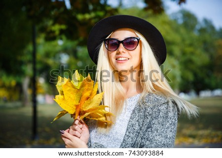 A nice girl with glasses is holding yellow foliage in her hands.