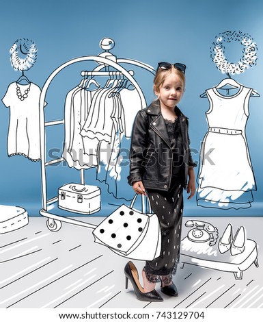 Stylish little girl in high heeled shoes, skirt and leather jacket holding bags while choosing clothes in drawn wardrobe