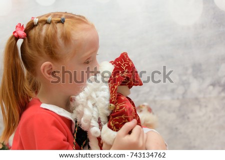 close up of little girl with Santa Claus costume on kissing a Father Christmas ornament on a blurred winter background