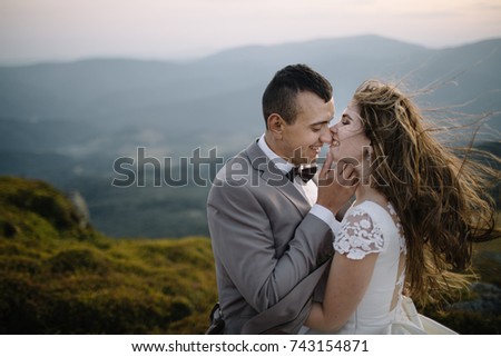 Happy gorgeous bride and groom walking in sun light holding hands, boho wedding couple, luxury ceremony at mountains with amazing view, space for text