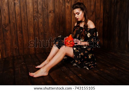 Black girl in dress with bright make-up and pumpkin against wooden background. Halloween theme.