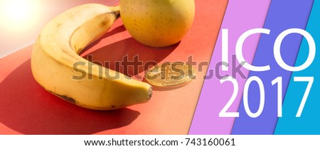 Banana, apple and golden bitcoin on the red background with multicolored stripes from right side with the letters: ICO 2017.
