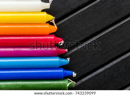 Many colorful candles in a single row and line, black background, candles of vibrant white. yellow, orange, red and blue colors, in a rainbow gradient